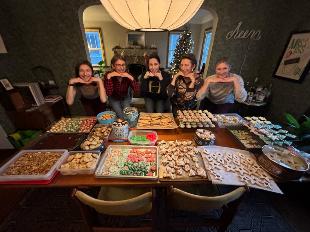 Friends gathered around a table filled with homemade holiday cookies